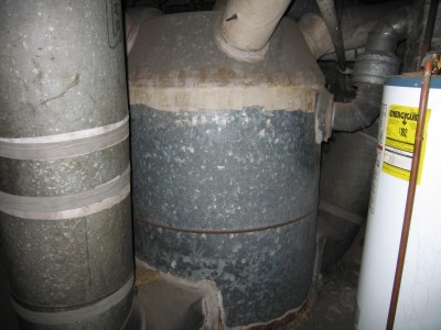 That off-white wrap on the top of the furnace and the pipes is asbestos! It used to be applied damp much like the old plaster-of-Paris casts on broken arms and legs. If you see white wrapping like this on your ducts do NOT disturb it. PHOTO CREDIT: Tony White